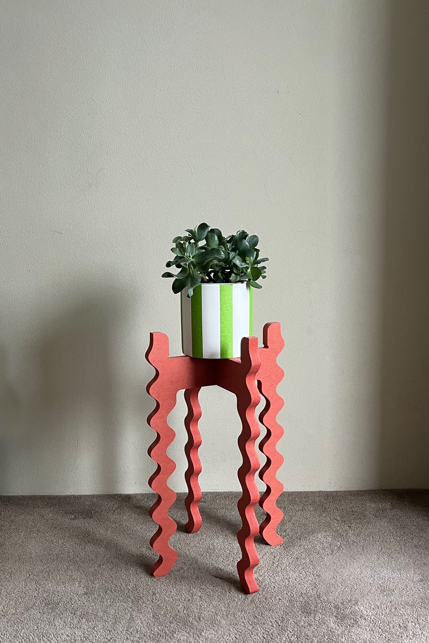 Red wavy Xigglie Poppy Tallboy Wide plant stand with a green plant and white pot against a plain wall.