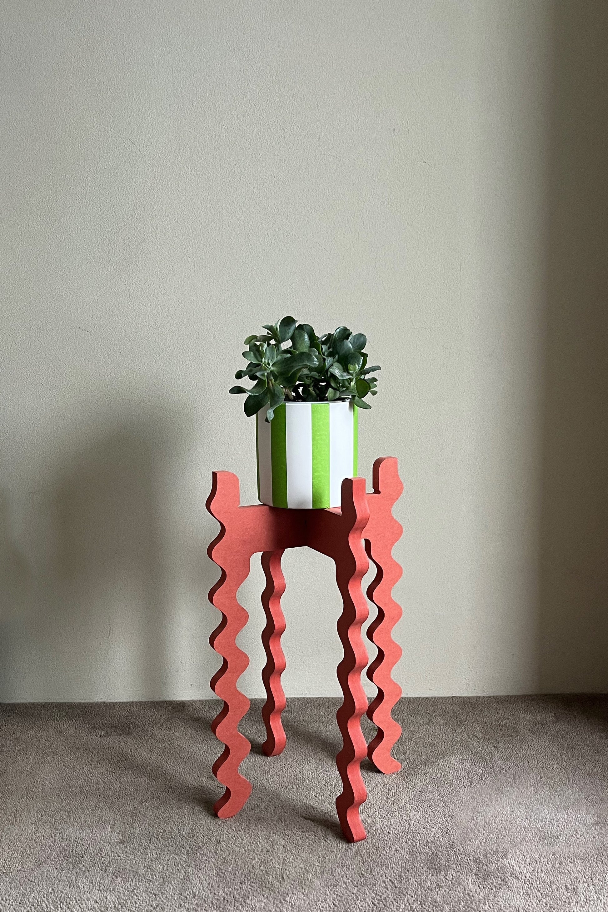 Red wavy Xigglie Poppy Tallboy Wide plant stand with a green plant and white pot against a plain wall.
