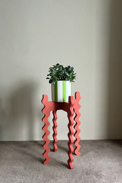 Red wavy Xigglie Poppy Tallboy Wide plant stand with a green plant and white pot against a plain wall.