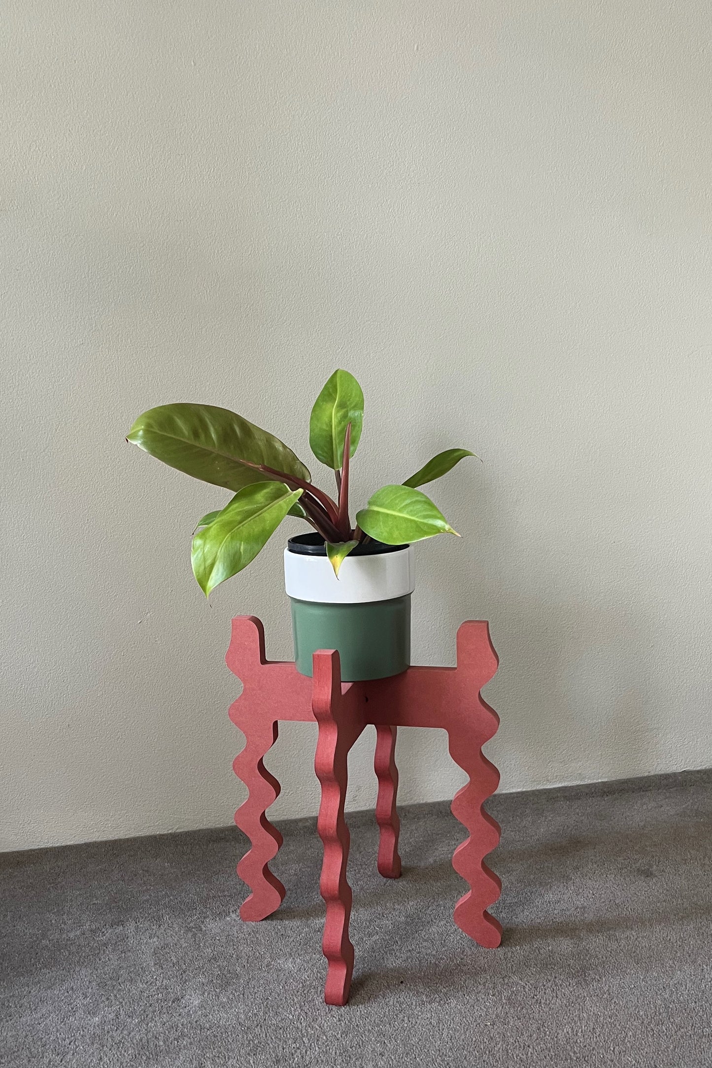 Potted plant on a red wavy Xigglie Poppy Middie Wide Plant Stand against a plain wall
