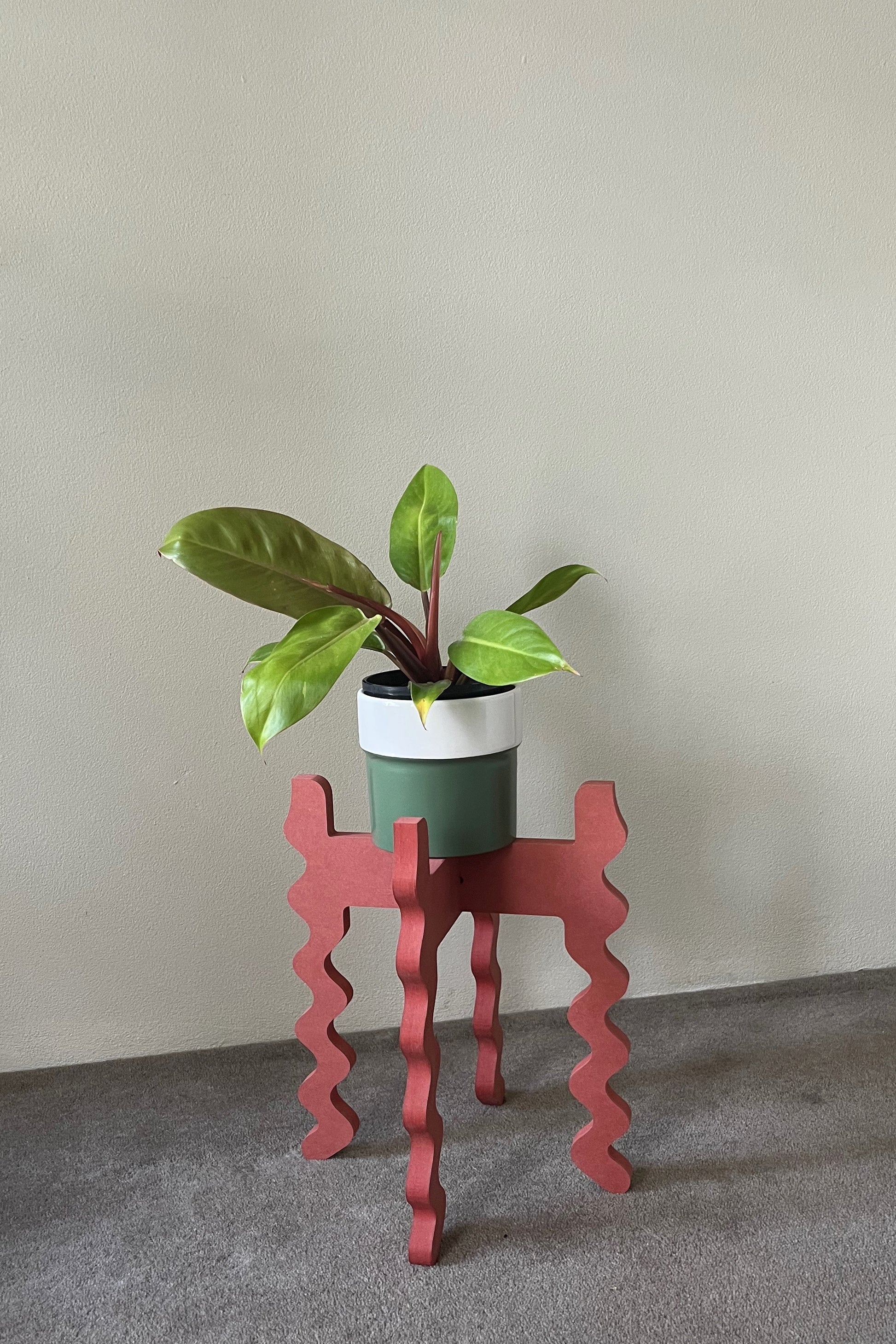 Potted plant on a red wavy Xigglie Poppy Middie Wide Plant Stand against a plain wall