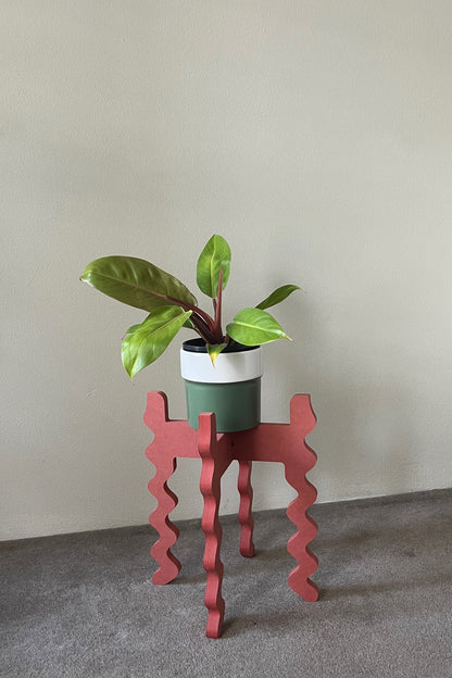Potted plant on a red wavy Xigglie Poppy Middie Wide Plant Stand against a plain wall