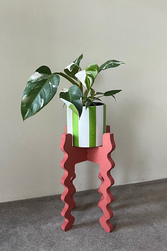 Potted plant on a red wavy Xigglie Poppy Middie Skinny Plant Stand against a plain wall