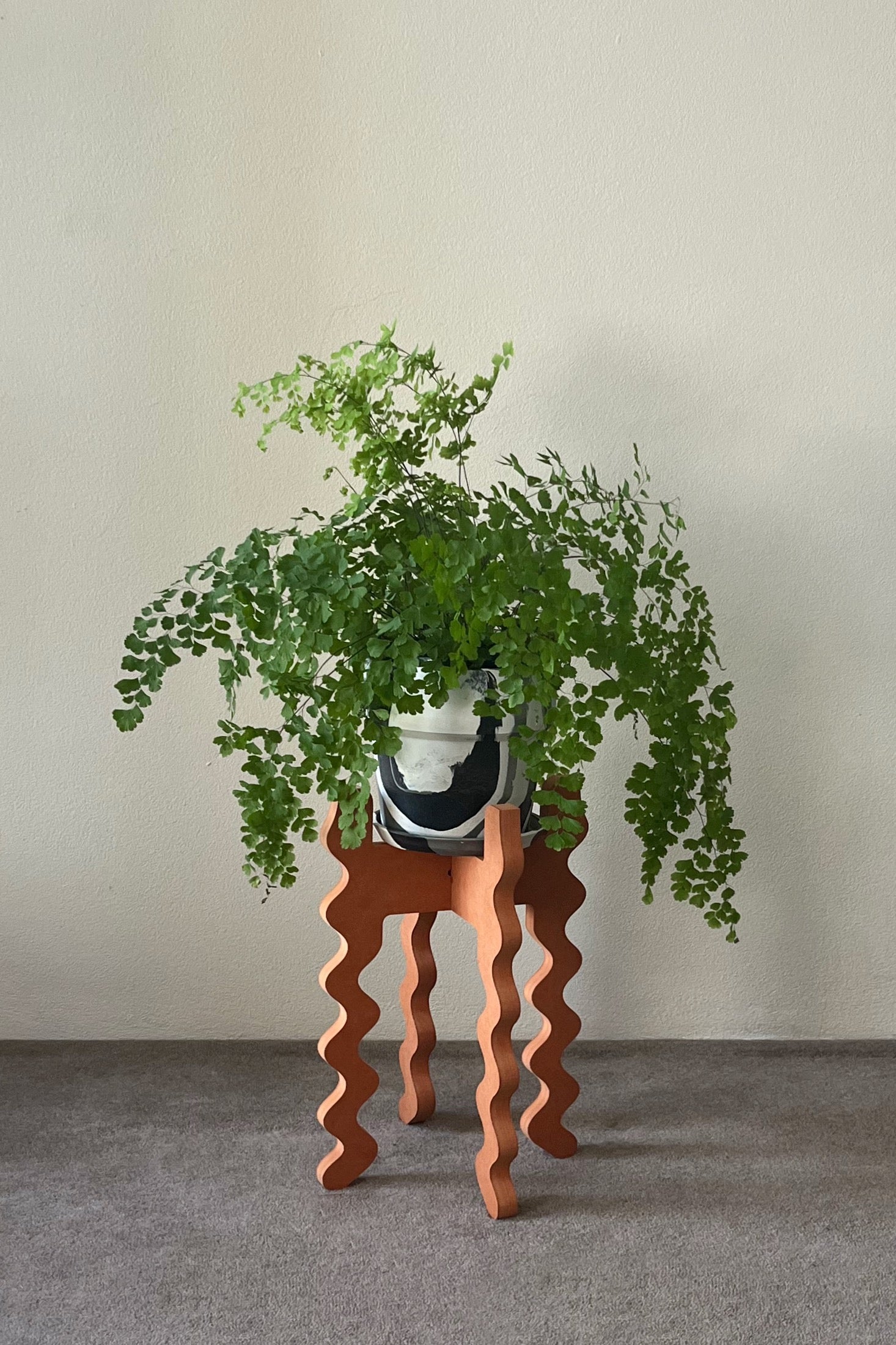 Potted plant on an orange wavy Xigglie Mango Middie Skinny Plant Stand against a plain wall